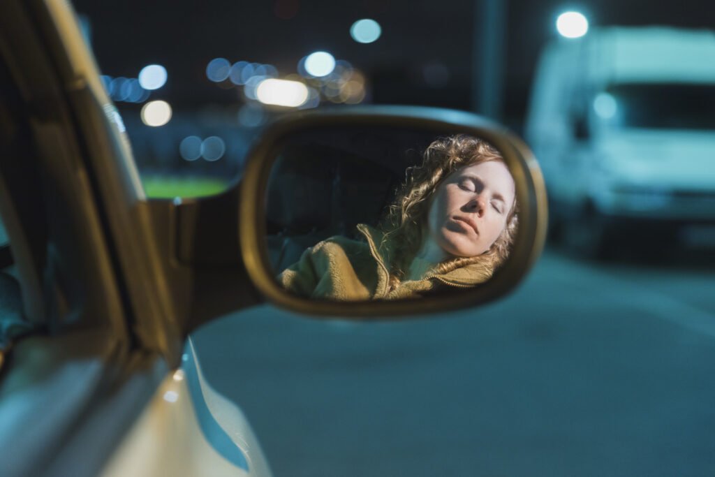 Moça dormindo em um estacionamento para recuperar-se do sono antes de seguir trajeto.