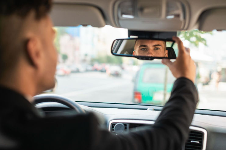 Motorista ajustando a direção de seu retrovisor interno no carro para evitar ponto cego.